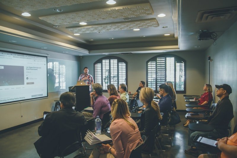 People seated in rows in a bright room, facing a presentation screen.